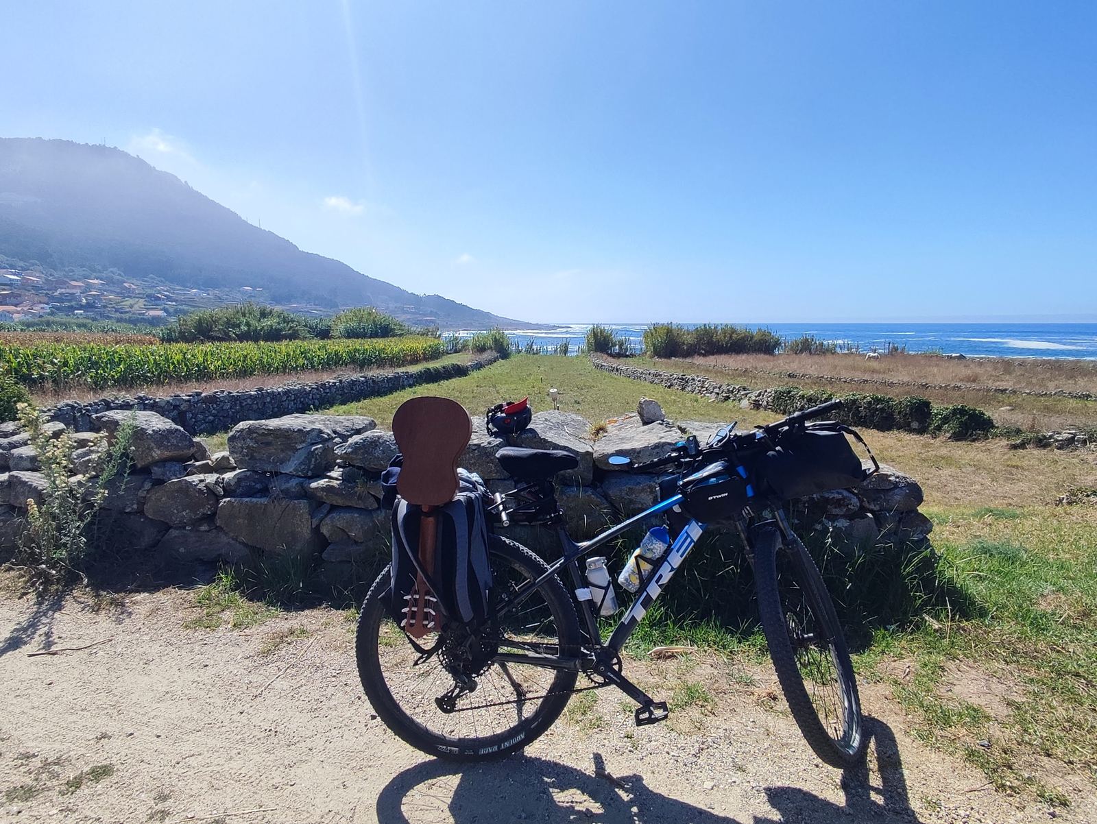 Two loaded bicycles leaning against a dry stone wall above maize fields running down to the Atlantic
