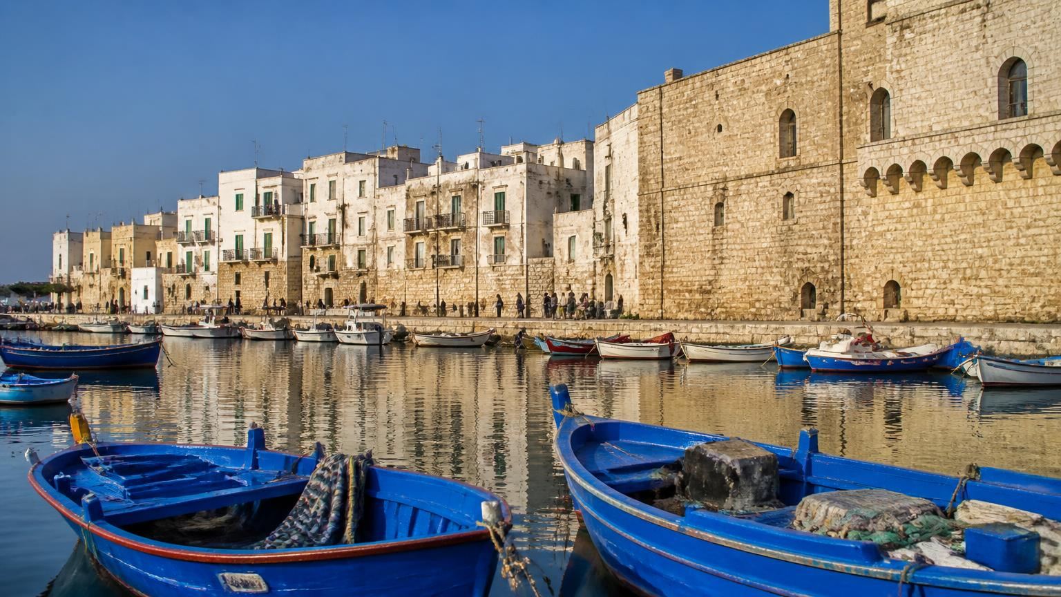 Monopoli harbour: blue wooden fishing boats moored below whitewashed houses and the fortress wall